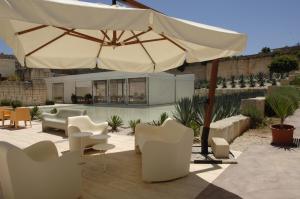 a patio with white chairs and an umbrella at Cave Bianche Hotel in Favignana
