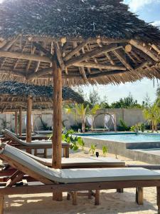 a group of lounge chairs under a straw umbrella next to a pool at Pamoja Villas in Migogoni