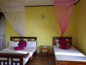 two beds in a room with yellow walls at Chamodya Home Stay in Ella