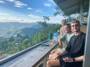a group of men sitting on a balcony with a view of mountains at Homestay Nunga หนูหง่าโฮมสเตย์กิกอคอ in Pang Mapha