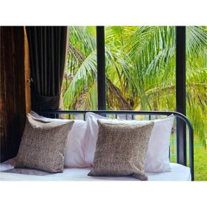 Ban Tha MaphraoにあるCheewatra Farmstay Coconut Houseの枕付きのベッドとヤシの木のある窓