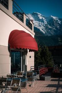 ヴェンゲンにあるHotel Victoria Lauberhorn Wengen, a Faern Collection Hotelの椅子と山が描かれた赤い日よけのあるパティオ +45枚の写真