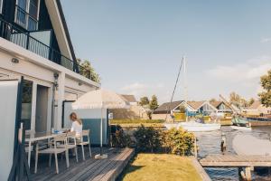 a woman sitting at a table on a deck next to a house at Herenhuis geschakeld | 8 personen - Boutique Parc Pharshoeke in Heeg