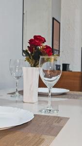 two wine glasses sitting on a table with a vase of roses at Apto bem localizado - com garagem in Salvador