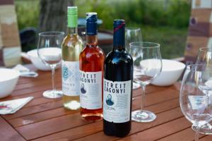 three bottles of wine sitting on a wooden table with glasses at Madárles in Tahitótfalu