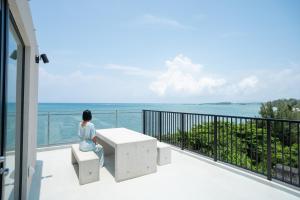 a woman sitting on a bench on a balcony looking at the ocean at TIMeSCAPE -tancha- in Onna