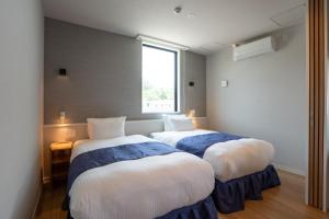 two beds in a room with a window at TIMeSCAPE -tancha- in Onna