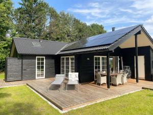 a black house with a deck with a table and chairs at Lovely Black Wooden House Near Tisvilde Hegn in Tisvilde