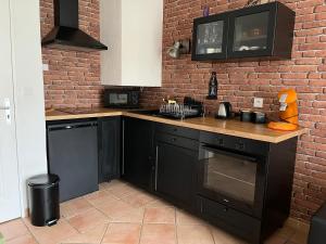 a kitchen with black cabinets and a brick wall at Cottage en duplex meublé au calme proche Orleans in Ardon