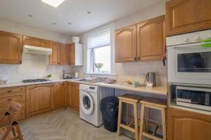 a kitchen with wooden cabinets and a washer and dryer at Ashgrove House - 3 bedroom in Coatbridge