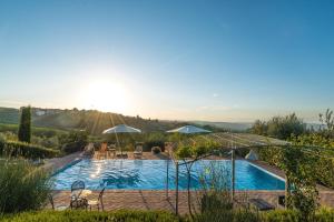 a swimming pool with chairs and umbrellas and the sunset at Villa i Colli in Montaione