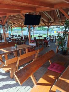 Un patio con bancos y mesas de madera y un televisor de pantalla plana. en Grill Terasz Étterem és Szálláshely, en Mezőkövesd