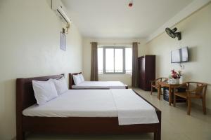 a bedroom with two beds and a desk and a television at Loan Ngạn Hotel Hải Hòa in Nghi Sơn