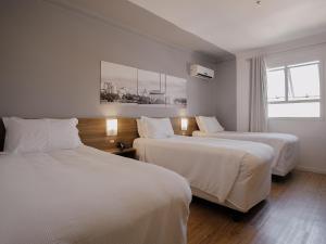 a hotel room with two beds and a window at Hotel Açores Premium- 5 minutos do Moinhos de Vento in Porto Alegre