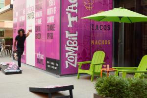 a man walking in front of a pink wall with chairs at Moxy Louisville Downtown in Louisville