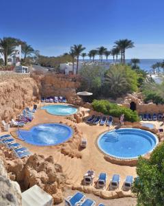 two pools on a beach with chairs and the ocean at Domina Coral Bay Elisir in Sharm El Sheikh