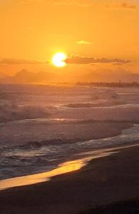 a sunset on the beach with the sun setting at Apartamento com vista para o mar de Ponta Negra, Maricá, RJ in Maricá