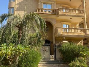 a yellow building with a gate and palm trees at The Gardenia Villa Chic Escape with Pool in 6th Of October