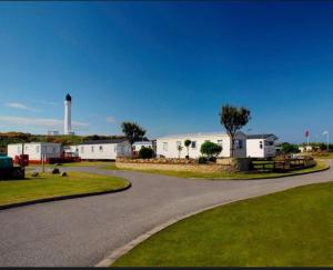 a winding road with a lighthouse in the background at Spacious Modern Seaside Caravan in Lossiemouth