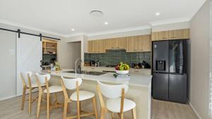 a kitchen with a island with white chairs and a black refrigerator at Coastal Drift in Callala Bay