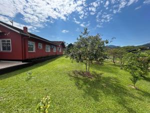 Un patio verde al lado de un edificio rojo con un árbol. en Morada dos Pomares, en Pomerode