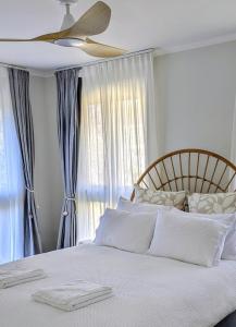 ein Schlafzimmer mit einem weißen Bett mit Deckenventilator in der Unterkunft Charming Coastal Cottage Retreat in Vincentia