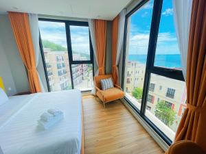 a bedroom with a bed and a chair and large windows at We Young Apartments by HOFs - Fireworks & Ocean view in Phú Quốc