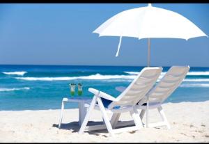 two chairs and a table with an umbrella on the beach at VISTA ESPETACULAR - TWIN TOWERS - Barra da Tijuca in Rio de Janeiro