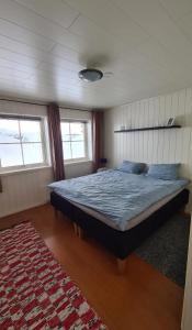 a bedroom with a bed and two windows and a rug at Sentrumsnær sokkelleilighet in Bardu