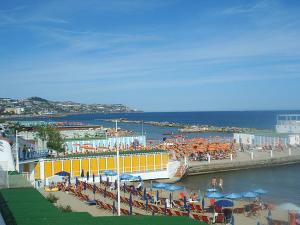 une plage avec des chaises et des parasols et un bâtiment jaune dans l'établissement Hotel Esperia, à Sanremo