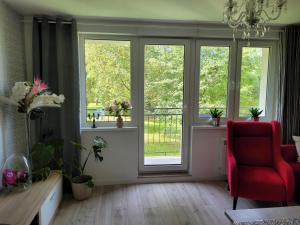 a living room with a red chair and windows at Apartament MILANO Chojnice in Chojnice