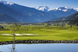 a golf course with a lake and snowy mountains at Apartment building, Fügen in Fügen
