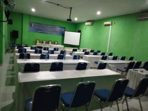 a conference room with white tables and chairs and a screen at Four Hostel Bandar Lampung in Tanjungkarang