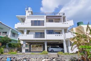 ein weißes Gebäude mit einem davor geparkten Auto in der Unterkunft Wind Henza - Vacation STAY 73122v in Uruma