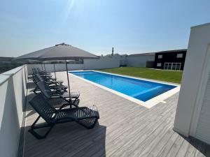 a deck with chairs and an umbrella next to a pool at Lugar do Paraíso - duas casas, uma só experiência - Vila do Conde in Touguinho