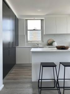a white kitchen with two bar stools and a sink at Elegant Beachfront Retreat with Fabulous Views in Sydney