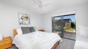 a white bedroom with a bed and a sliding glass door at One Mile Retreat in Anna Bay