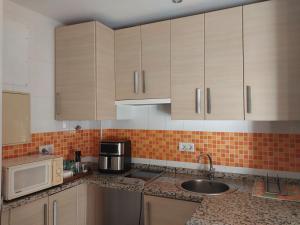 a kitchen with wooden cabinets and a sink and a microwave at Ático acogedor, céntrico y a 2 min de la playa. in Fuengirola