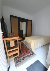 a bedroom with a bed and a desk with a television at Quarto c banheiro para uma pessoa in Poços de Caldas