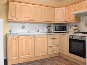 a kitchen with wooden cabinets and a sink and a microwave at Swallow Cottage - Uk49756 in Little Singleton