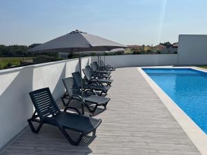 a row of chairs with an umbrella next to a swimming pool at Lugar do Paraíso - duas casas, uma só experiência - Vila do Conde in Touguinho