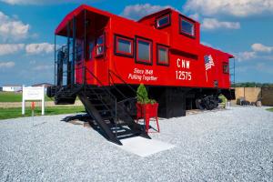 a red train car sitting on display on gravel at Cozy Caboose Retreat | Sleeps 4 | Fire Pit in Fredericktown