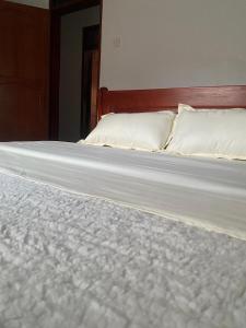 un letto con lenzuola bianche e cuscini sopra di Paradise pathways lweza a Mutungo