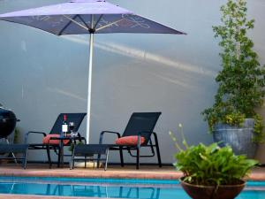 three chairs and a table with an umbrella next to a pool at The Lantern Guesthouse in Bloemfontein
