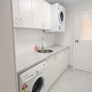 a white kitchen with a sink and a washing machine at 3 Bedroom Deluxe Family Home in Rooty Hill +14 photos