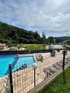 a swimming pool with chairs and a river in the background at Apto Itaipava 5 min do Centro e Parque de Eventos in Itaipava
