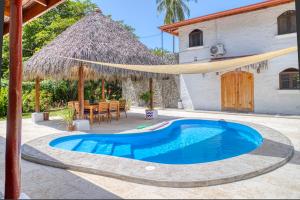 a swimming pool in front of a house with a thatch roof at Mariposa Monarca in Esterillos