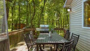 a wooden table and chairs on a deck with trees at Lake Daze by AvantStay Lakefront w Modern Interior Enclosed Porch Hot Tub in Long Pond