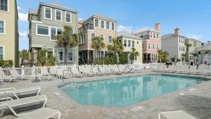 a swimming pool with chaises and chairs in front of houses at 109 Grand Pavilion by AvantStay Beachfront Views in Isle of Palms