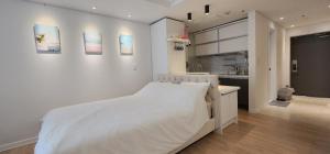 a white bedroom with a large bed and a kitchen at Marine City Cozy Stay in Busan